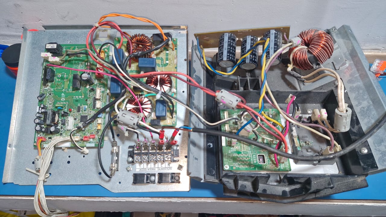An open inverter drive unit on a sturdy anti-static mat, revealing its intricate power electronics: large capacitors, IGBT modules, heat sinks, and neatly routed wiring. A frequency inverter module stands upright beside it, its terminal block clearly visible. The setting is a modern electronics lab in Rio de Janeiro, suggested by a distant window view of hazy hills and urban buildings, softly out of focus. Cool white LED bench lights illuminate the components, creating sharp clarity and defined highlights on metal surfaces. The composition uses rule of thirds with the main inverter in sharp focus and diagnostic instruments like an oscilloscope and power analyzer subtly blurred in the background. The atmosphere is precise, trustworthy, and technical, conveying deep expertise in inverter and frequency drive maintenance with realistic photographic detail.